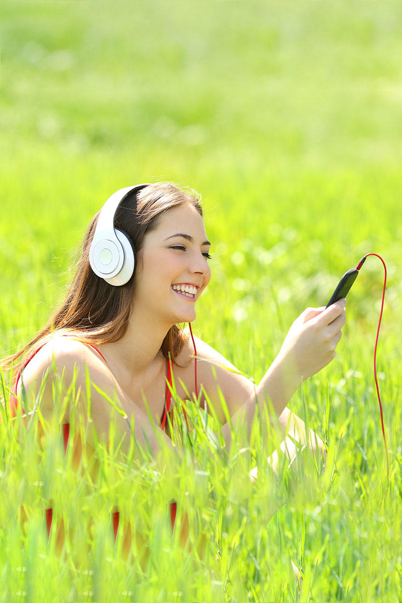 草地里戴白色耳机看手机的外国女性高清摄影图片